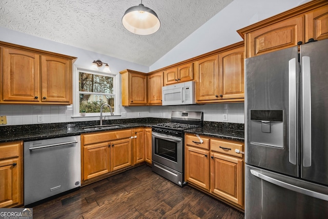 kitchen featuring lofted ceiling, sink, dark stone countertops, dark hardwood / wood-style flooring, and stainless steel appliances