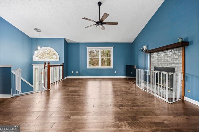 unfurnished living room with lofted ceiling, ceiling fan with notable chandelier, a brick fireplace, dark hardwood / wood-style floors, and a textured ceiling