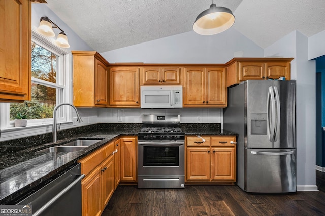 kitchen with sink, dark hardwood / wood-style flooring, dark stone counters, vaulted ceiling, and appliances with stainless steel finishes