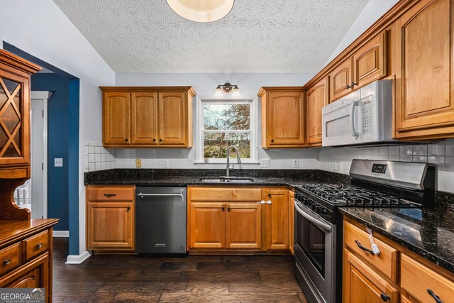 kitchen featuring sink, stainless steel appliances, dark hardwood / wood-style floors, dark stone counters, and a textured ceiling