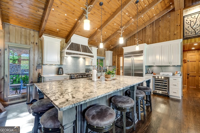 kitchen featuring a large island, beverage cooler, hanging light fixtures, stainless steel built in refrigerator, and white cabinets