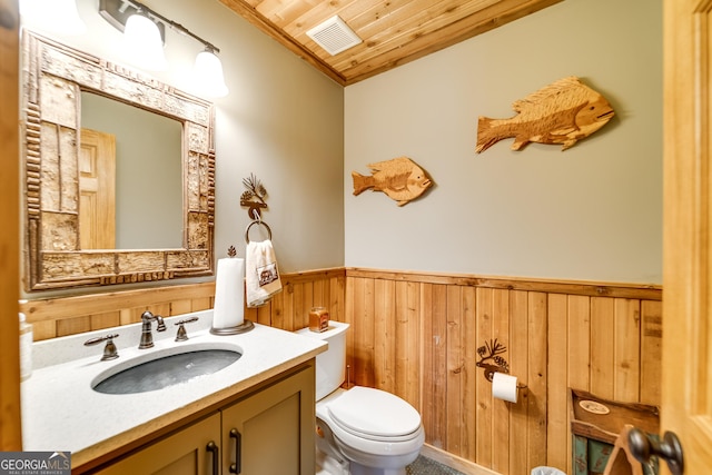 bathroom featuring wooden ceiling, wood walls, toilet, vanity, and ornamental molding