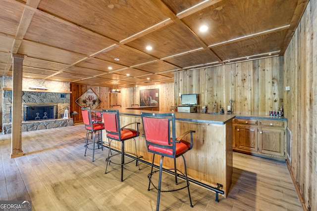 bar featuring light wood-type flooring, coffered ceiling, wood ceiling, a fireplace, and wood walls