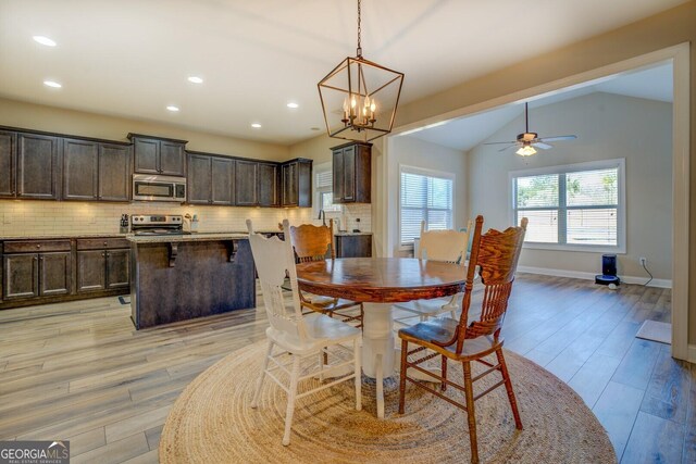 dining space with vaulted ceiling, ceiling fan with notable chandelier, and light hardwood / wood-style flooring