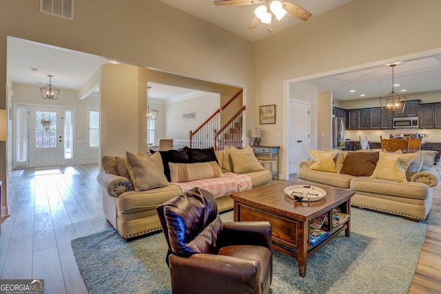 living room with vaulted ceiling, ceiling fan with notable chandelier, and light wood-type flooring