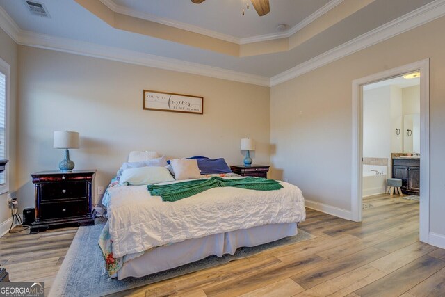 bedroom featuring ornamental molding, ceiling fan, a tray ceiling, ensuite bath, and light hardwood / wood-style flooring