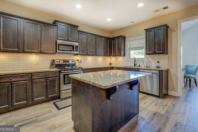 kitchen with sink, appliances with stainless steel finishes, light stone countertops, light hardwood / wood-style floors, and a kitchen island