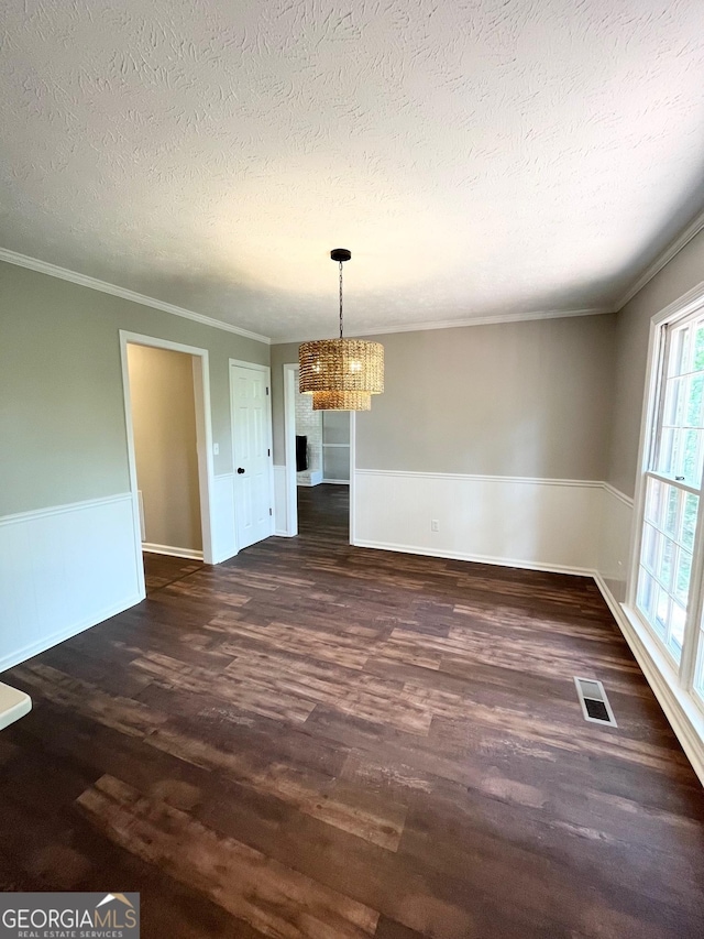 unfurnished dining area with a textured ceiling, dark hardwood / wood-style flooring, crown molding, and a chandelier