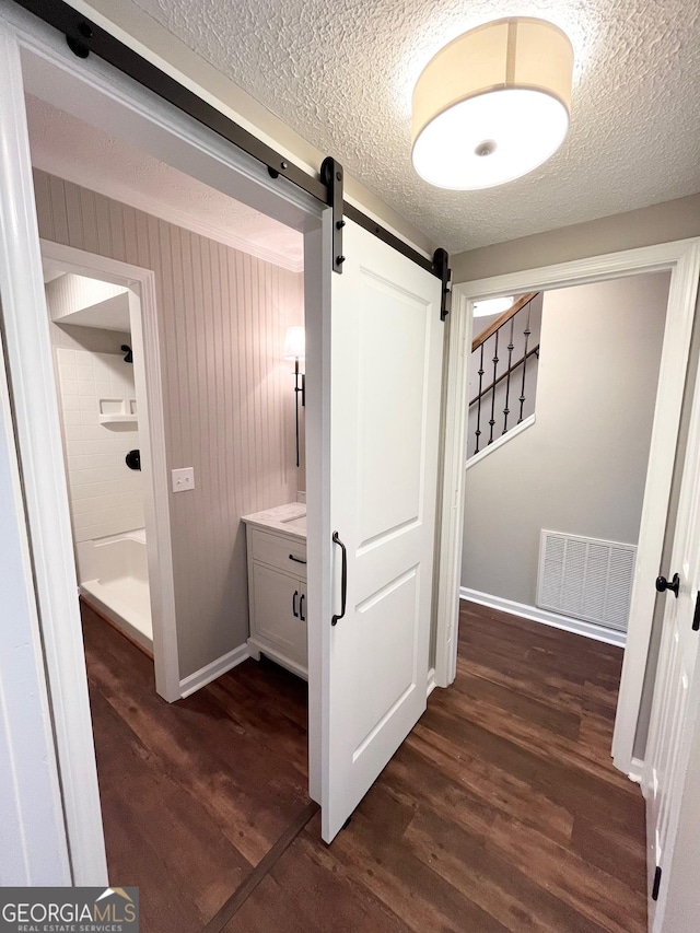 hallway with dark hardwood / wood-style flooring, a barn door, and a textured ceiling