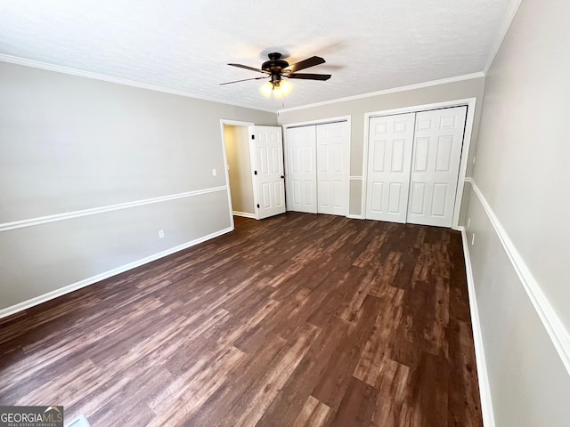 unfurnished bedroom with ceiling fan, dark hardwood / wood-style floors, crown molding, a textured ceiling, and two closets