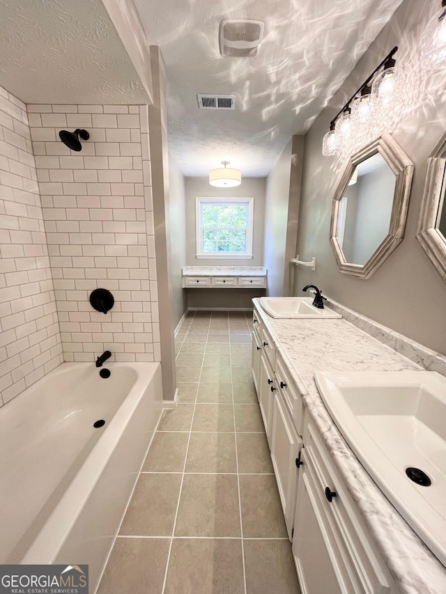 bathroom featuring vanity, a textured ceiling, tile patterned floors, and tiled shower / bath