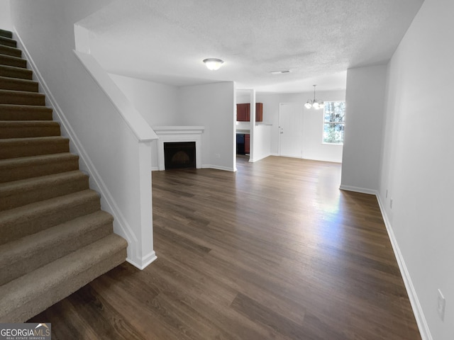 unfurnished living room with dark hardwood / wood-style flooring, a textured ceiling, and an inviting chandelier