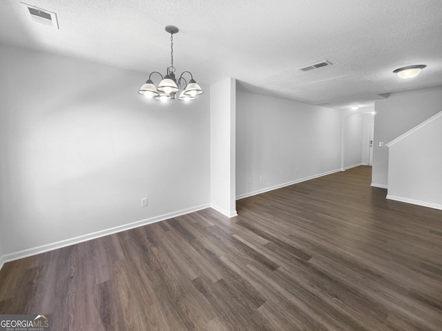 empty room featuring a notable chandelier, dark hardwood / wood-style floors, and a textured ceiling