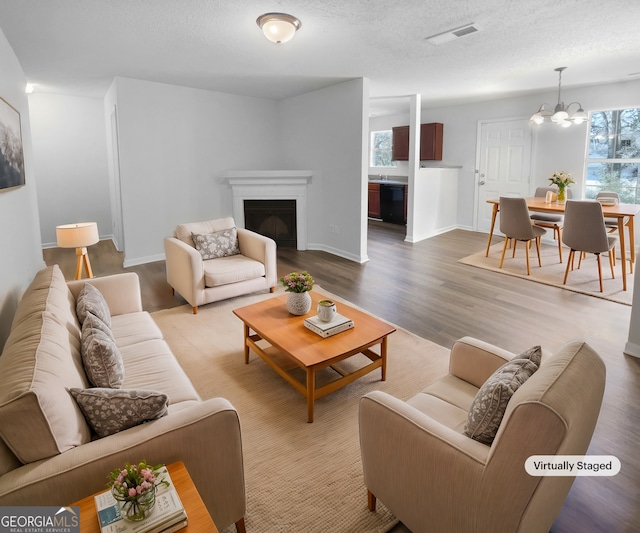 living room with hardwood / wood-style floors, a textured ceiling, an inviting chandelier, and a healthy amount of sunlight