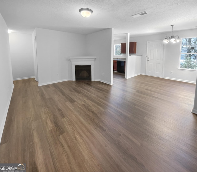 unfurnished living room with a chandelier, a textured ceiling, and dark wood-type flooring