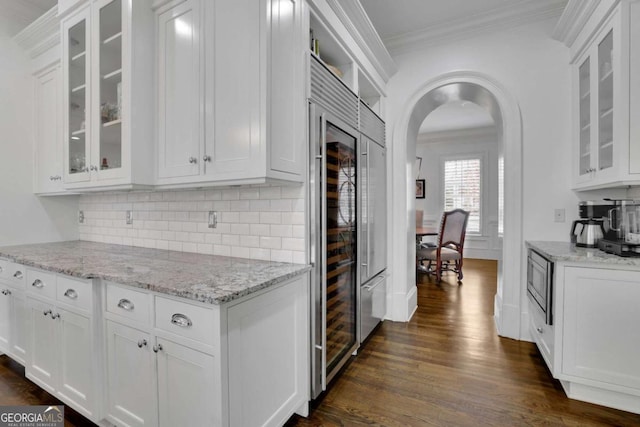 kitchen with dark wood-type flooring, decorative backsplash, ornamental molding, light stone counters, and white cabinetry