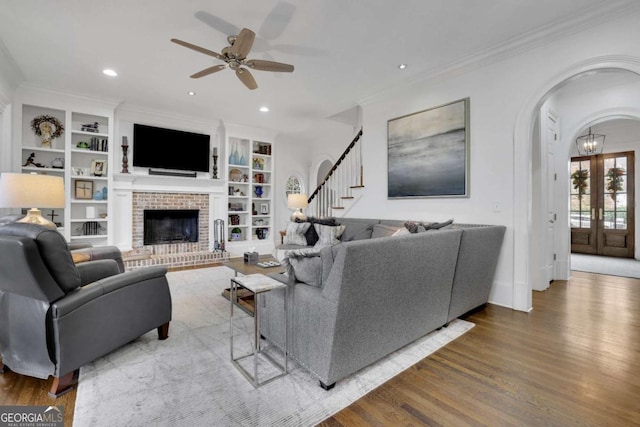 living room featuring ornamental molding, built in shelves, ceiling fan, a fireplace, and hardwood / wood-style floors