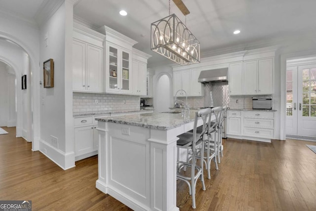 kitchen with white cabinets, extractor fan, a kitchen island with sink, and sink