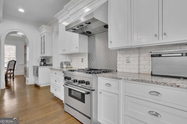 kitchen with light stone countertops, wall chimney exhaust hood, high end stove, built in microwave, and white cabinetry