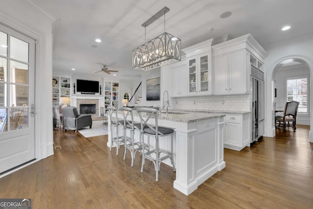 kitchen with white cabinets, sink, light stone countertops, an island with sink, and decorative light fixtures