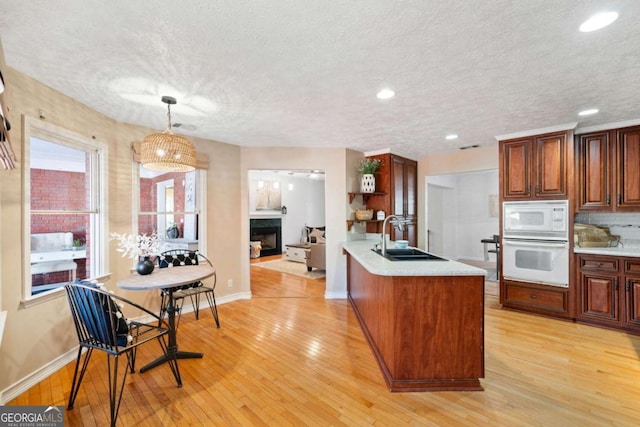 kitchen with sink, pendant lighting, a textured ceiling, white appliances, and light hardwood / wood-style floors