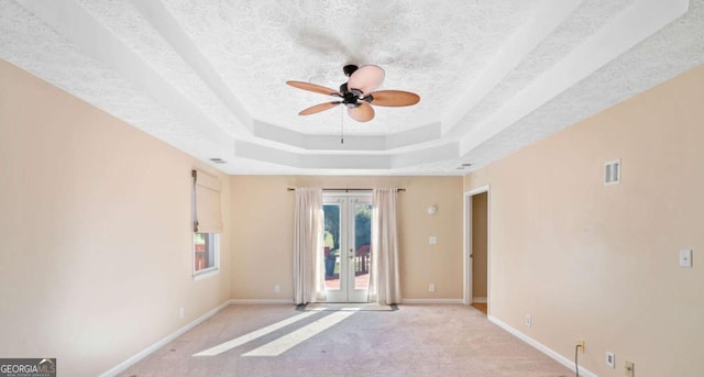 carpeted empty room with ceiling fan, a textured ceiling, a tray ceiling, and french doors