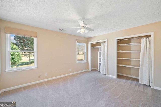 unfurnished bedroom featuring a textured ceiling, two closets, ceiling fan, and light colored carpet