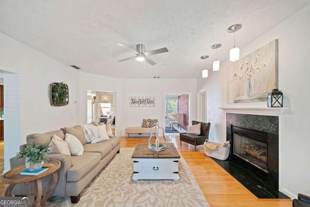 living room with a high end fireplace, wood-type flooring, a textured ceiling, and ceiling fan