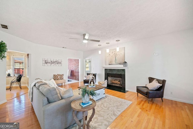 living room featuring ceiling fan, a healthy amount of sunlight, light hardwood / wood-style flooring, a high end fireplace, and a textured ceiling