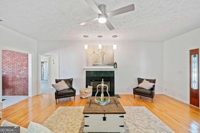 living room featuring ceiling fan with notable chandelier, hardwood / wood-style floors, a textured ceiling, and a premium fireplace