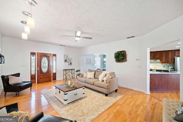 living room with a textured ceiling, light hardwood / wood-style flooring, ceiling fan, and sink