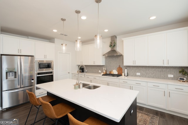 kitchen featuring wall chimney exhaust hood, sink, stainless steel appliances, and an island with sink