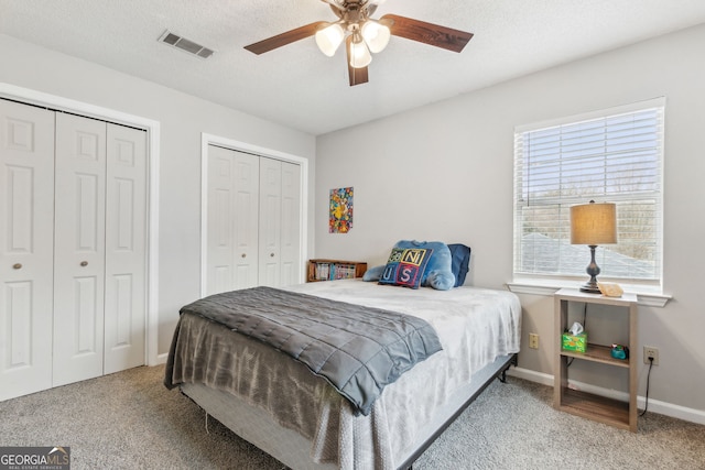 bedroom with ceiling fan, carpet floors, and two closets