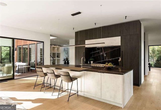 kitchen with pendant lighting, a breakfast bar, a center island with sink, sink, and light hardwood / wood-style flooring