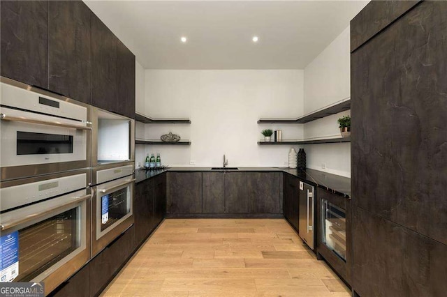 kitchen with sink, dark brown cabinets, light hardwood / wood-style floors, stainless steel double oven, and beverage cooler