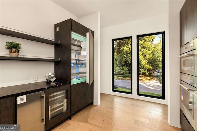 kitchen with dark brown cabinetry, wine cooler, and light hardwood / wood-style flooring