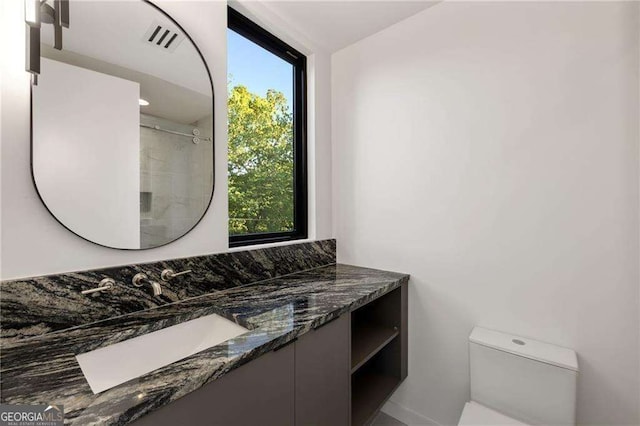 bathroom with walk in shower, vanity, and toilet