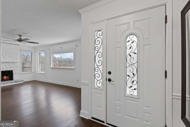 entrance foyer featuring a stone fireplace, crown molding, ceiling fan, dark hardwood / wood-style floors, and a textured ceiling