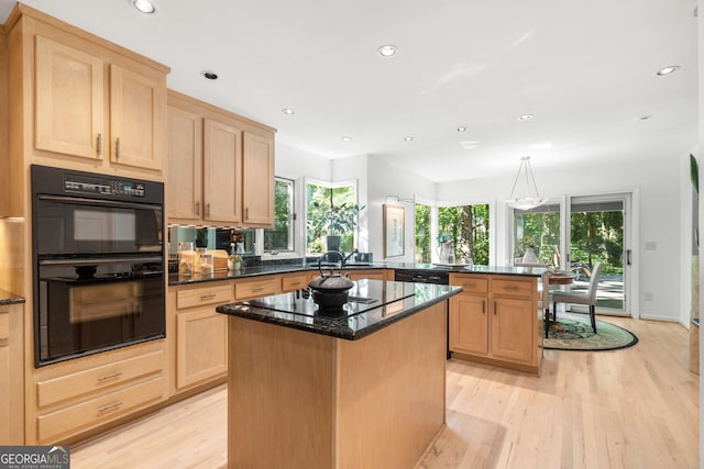 kitchen with kitchen peninsula, dark stone counters, black appliances, light hardwood / wood-style flooring, and a center island