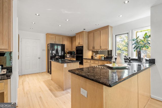 kitchen with a center island, black appliances, light hardwood / wood-style flooring, dark stone countertops, and kitchen peninsula