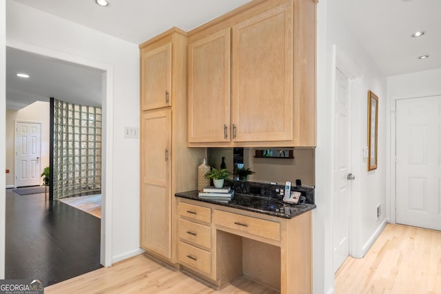 kitchen with light brown cabinets, light wood-type flooring, and dark stone counters