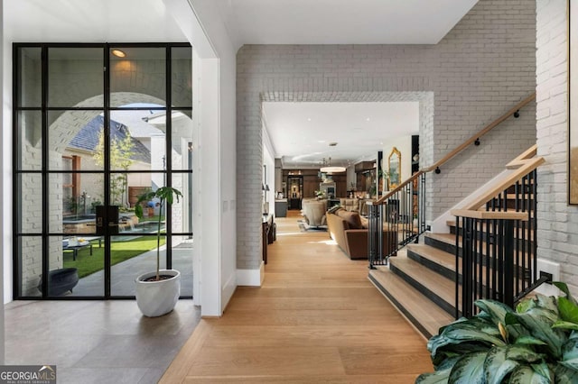 foyer entrance with floor to ceiling windows, brick wall, and light hardwood / wood-style flooring