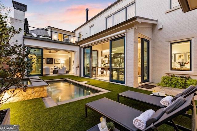 back house at dusk with a balcony and a yard