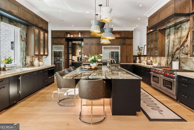 kitchen with a breakfast bar, high end appliances, a kitchen island with sink, sink, and hanging light fixtures