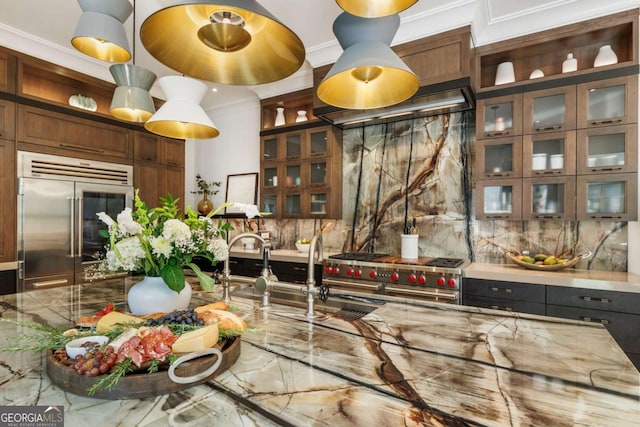 kitchen featuring crown molding, high end appliances, light stone counters, and range hood