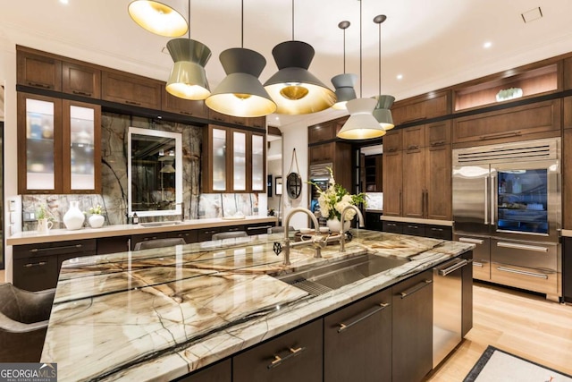 kitchen featuring sink, light hardwood / wood-style floors, light stone counters, and hanging light fixtures