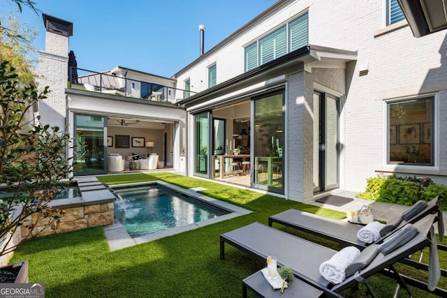 rear view of house with pool water feature, a balcony, and a lawn