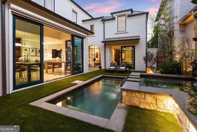 back house at dusk featuring pool water feature and a yard