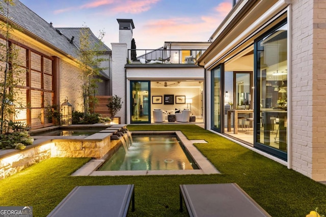 pool at dusk with an in ground hot tub, pool water feature, and a lawn