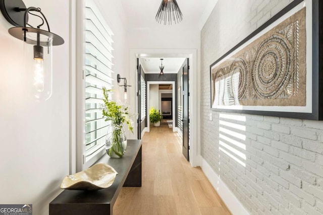 corridor with light hardwood / wood-style floors, ornamental molding, and brick wall